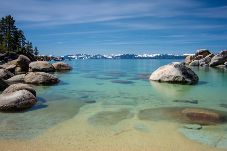 view of lake tahoe with turqoise waters, rock formations and snowcapped mountains in background