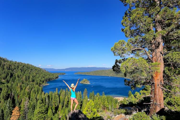 woman standing atop a hill overlooking Lake Tahoe with her arms raised in celebration