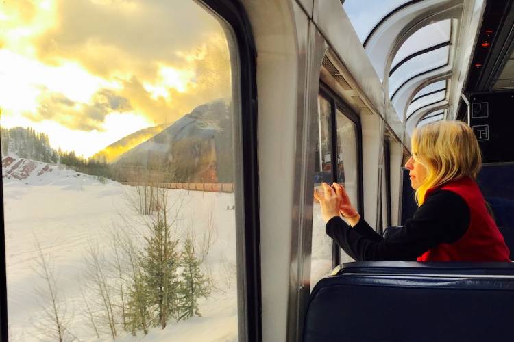 woman on an amtrak taking picture out the window of snowy peaks