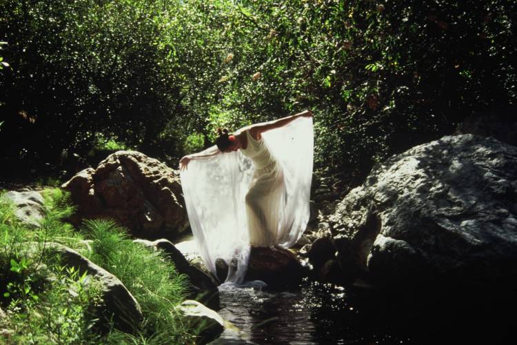 Woman in white posing on rocks over a river