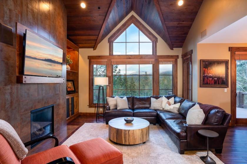 A vacation rental interior with high ceilings, a fireplace, and mountain views through the window in the background