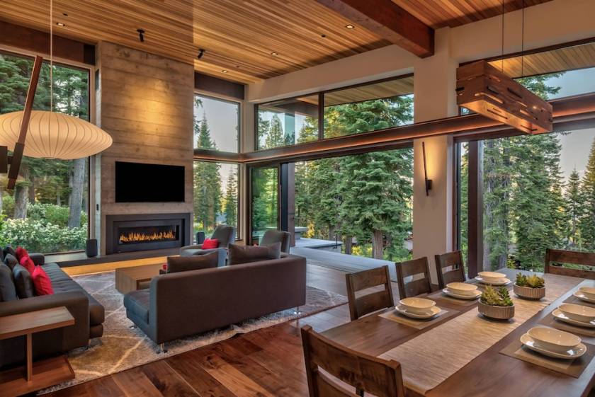 Vacation rental interior with high ceilings, a fireplace, and large picture windows opening up to green forest views