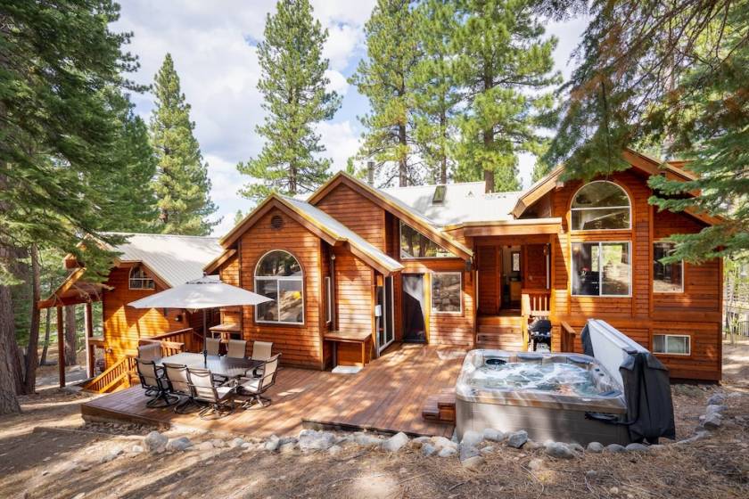 Lodge-style vacation rental exterior with furnished deck and private hot tub in a wooded setting