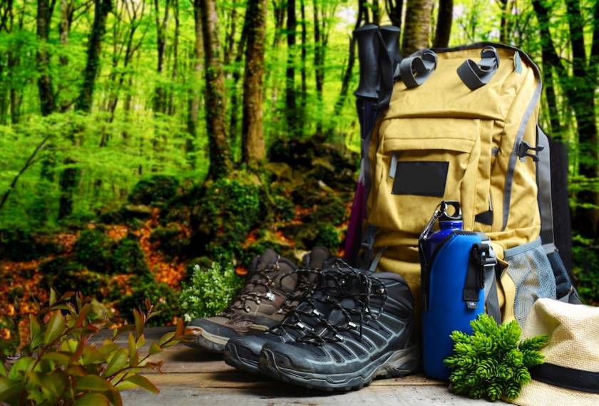 hiking gear on display featuring a yellow backpack, boots, a water bottle in a wooded scene