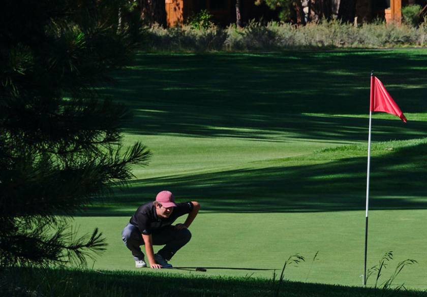 man kneeling on golf course looking at ball going into hole