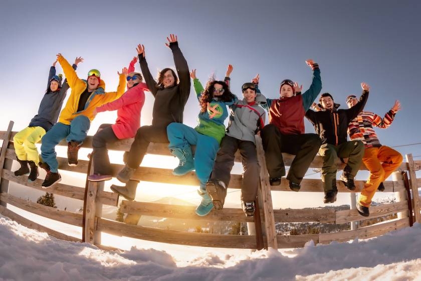 group of young people sitting on a fence at a ski resort 