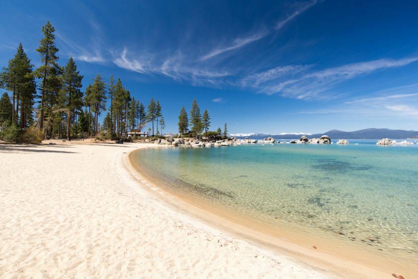 pristine white beach with crystal clear water and pine trees with blue skies in lake tahoe california