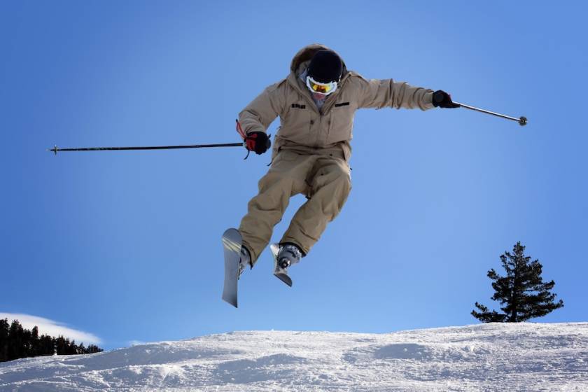 A skier mid-jump with fresh snow and a clear, blue sky in the background